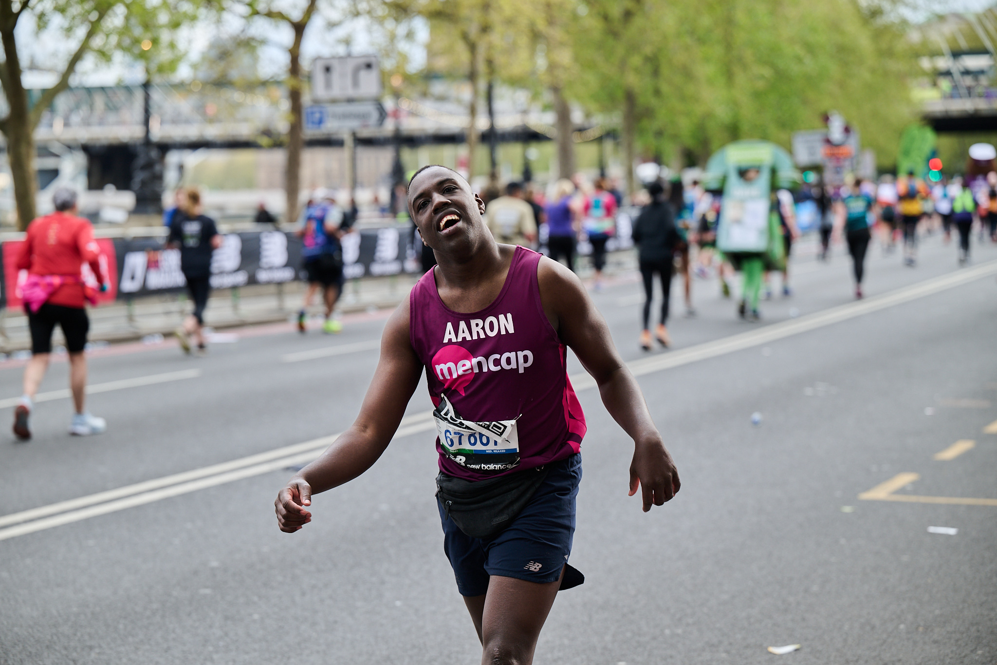 Aaron a runner with a learning disability running the London Marathon wearing a Mencap running vest and smiling.