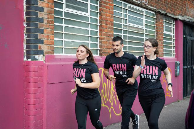 Two young women and one young man running together outside whilst wearing black "Run with us" t-shirts.